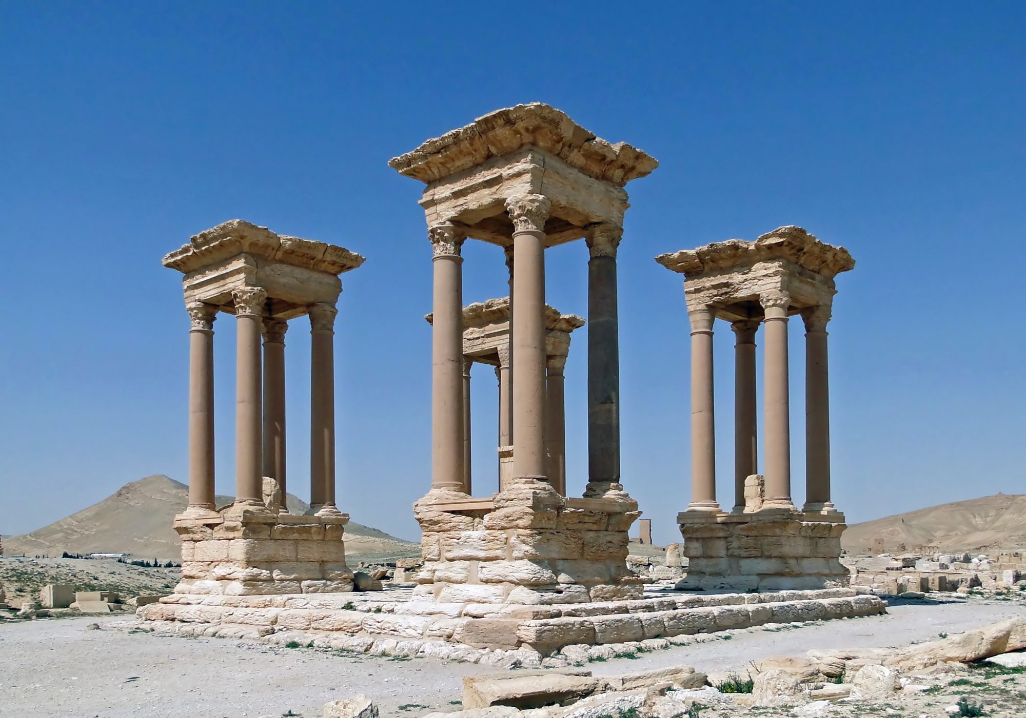 Tetrapylon i Palmyra, fire søjlegrupper på en fælles sokkel, med ørken og bakker bagved.